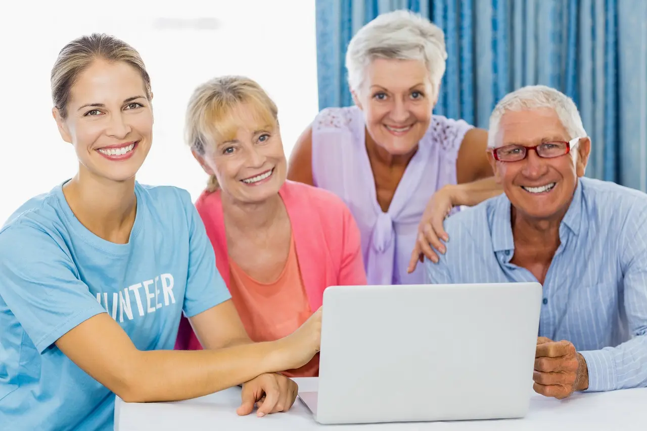 Vier Personen sitzen vor einem Laptop und lachen in die Kamera