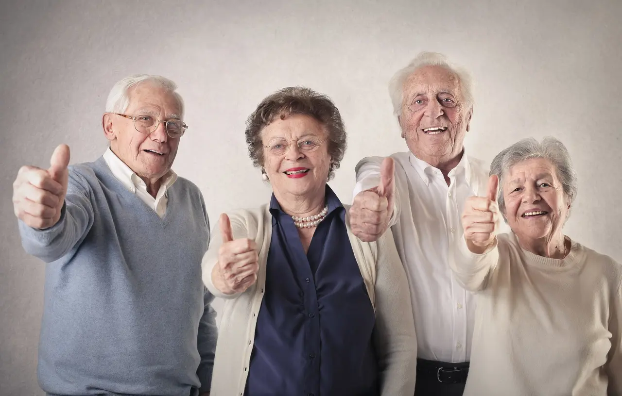 Vier Senioren lachen in die Kamera und strecken ihren Daumen nach oben